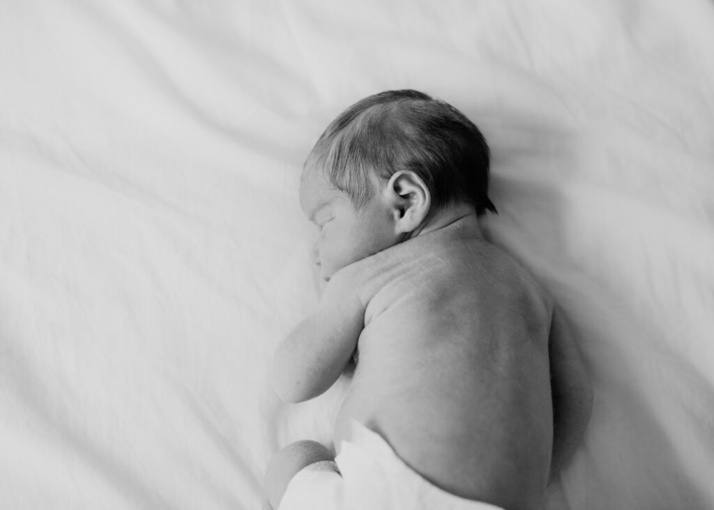 newborn baby curled up on bed
