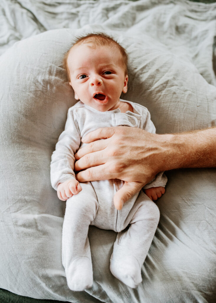 A gentle hand holds yawning newborn baby boy 