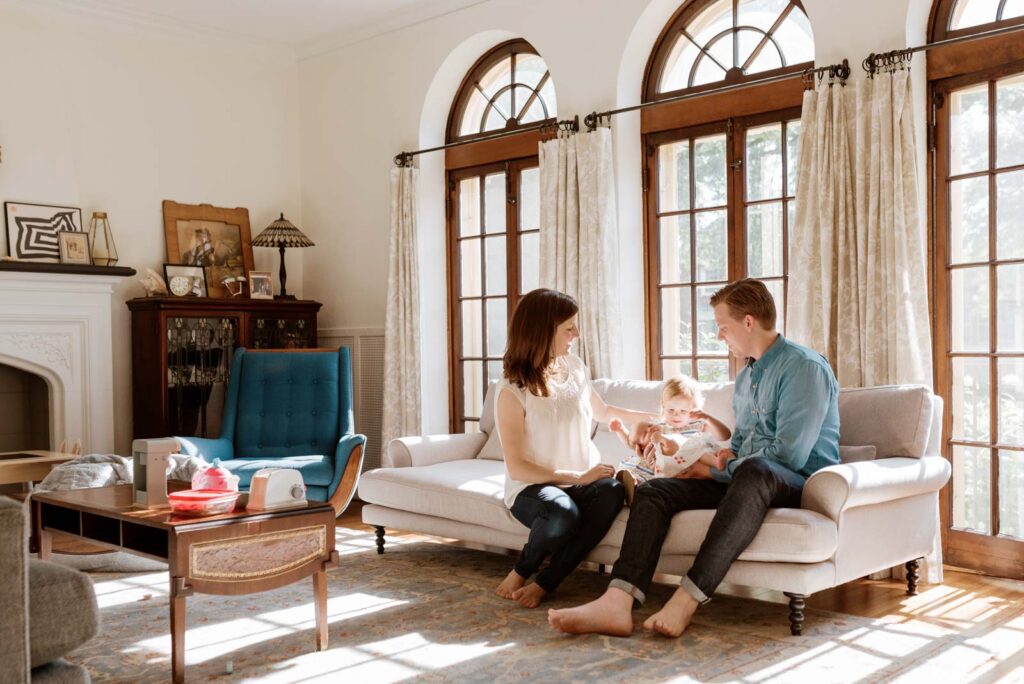 Parents sit in their living room with their newborn and two year old daughter